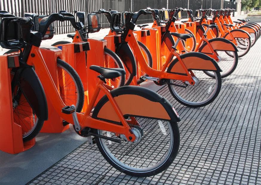 Hilera de bicicletas urbanas naranjas ancladas en una estación de la ciudad