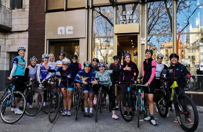 Grupo de mujeres ciclistas reunidas con sus bicicletas frente a una tienda